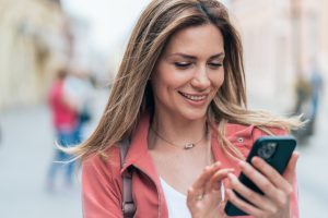 Cheerful young woman texting outdoor in the city. Happy woman using smartphone on the street. Happy to be Connected always and everywhere,