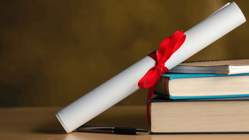 En pappersrulle knuten med ett rött band står lutad mot en trave böcker.